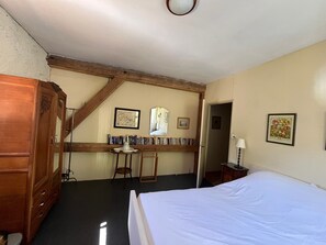 Ein Schlafzimmer mit Bett, einem Holzschrank, einem Schreibtisch mit Büchern und einem gerahmten Bild an der Wand.