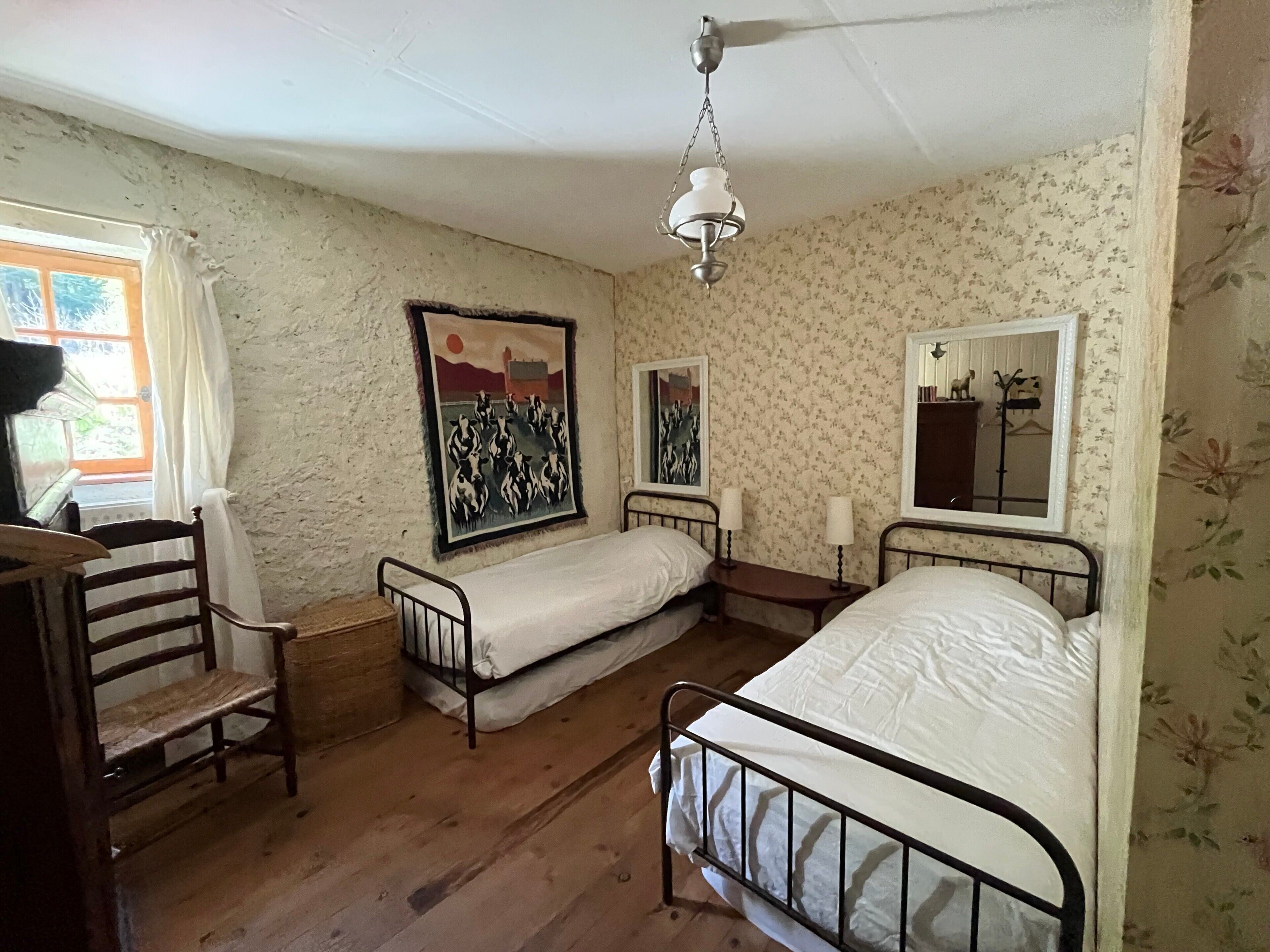 Une chambre avec deux lits simples, une chaise en bois, un bureau et un luminaire suspendu.