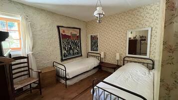 Une chambre avec deux lits simples, une chaise en bois, un bureau et un luminaire suspendu.