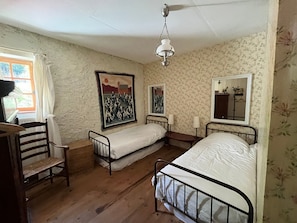 Una habitación con dos camas individuales, una silla de madera, un escritorio y una lámpara colgante.