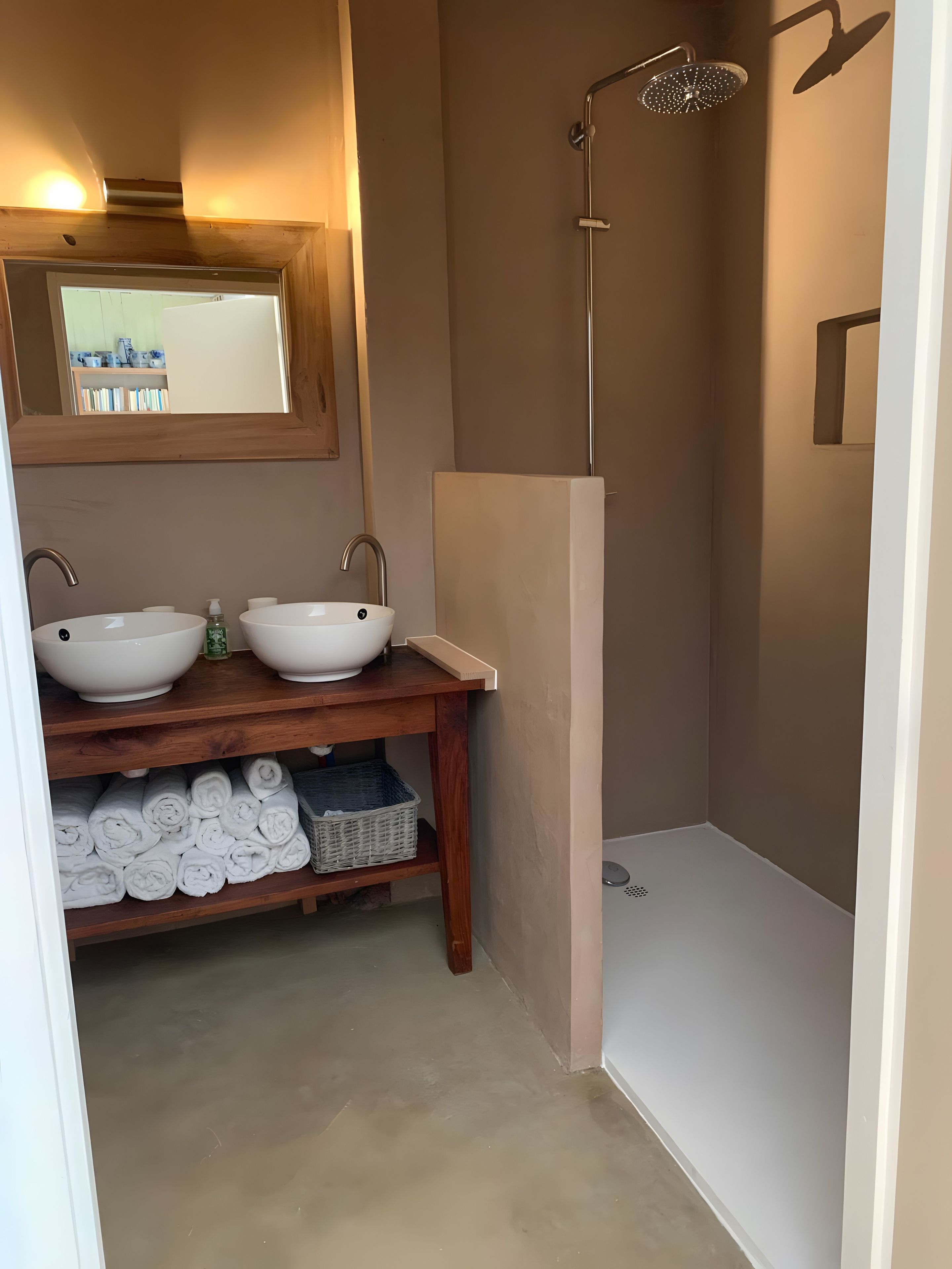 Ein Badezimmer mit zwei Waschbecken, einer Dusche und einem hölzernen Ablagefach mit Handtüchern.