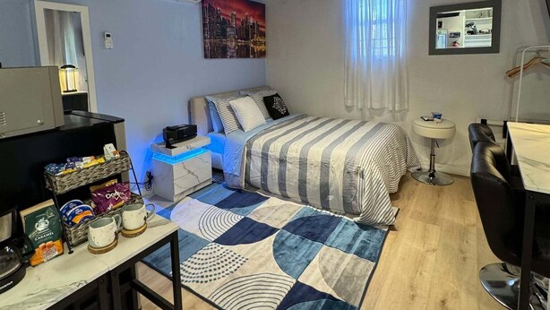 Quarto com cama, mesa de cabeceira, abajur e escrivaninha com cadeira.