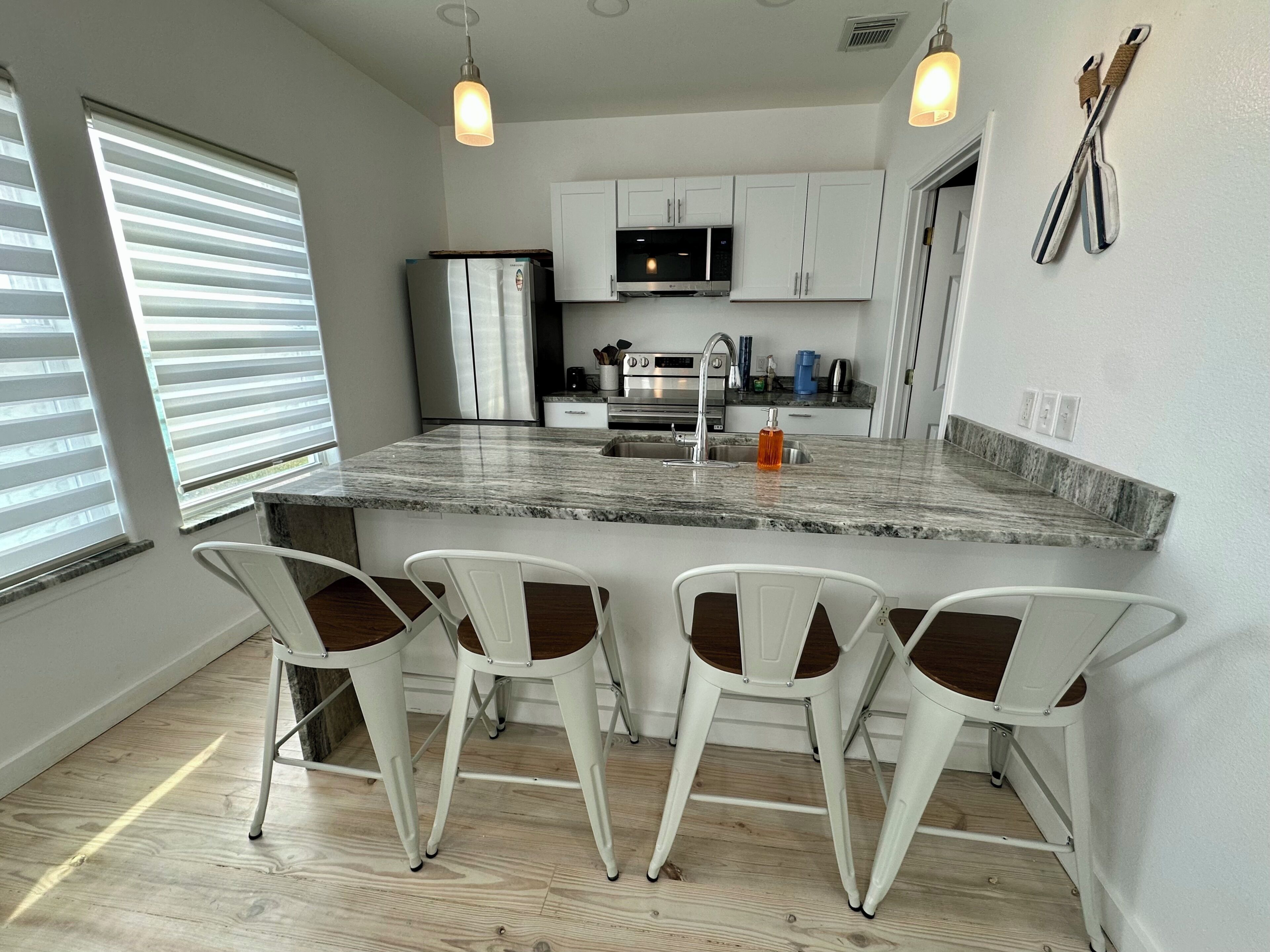 A modern kitchen with a central island, white cabinetry, and bar-style chairs.