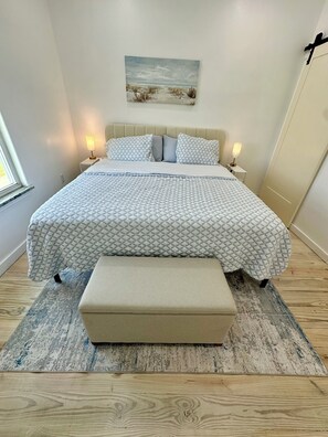 Een slaapkamer met een bed, nachtlampjes, een schilderij en een bankje.