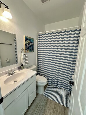 Een badkamer met een wit wastafel, een toilet, een gestreept douchegordijn, een handdoekhouder, een spiegel en een schilderij aan de muur.