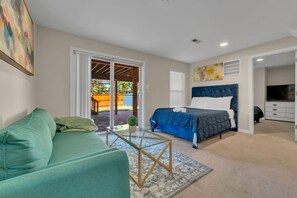 A bedroom with a bed, a green sofa, a glass coffee table, and a TV.