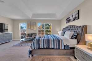 Un dormitorio con una cama grande, televisión, cómoda y ventana con vista a árboles.