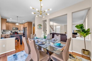Cocina moderna con mesa de futbolín, comedor con mesa y sillas de vidrio y una planta grande en maceta.