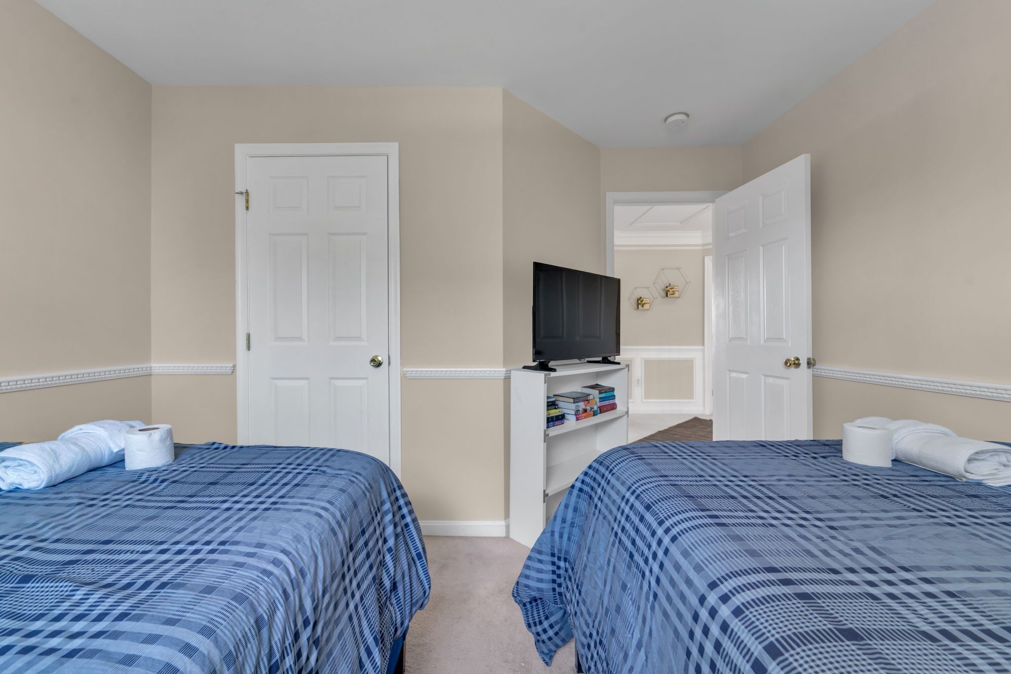 A hotel room with two beds, a television, and a small shelf with books.