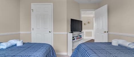 Habitación de hotel con dos camas, televisión y un pequeño estante con libros.