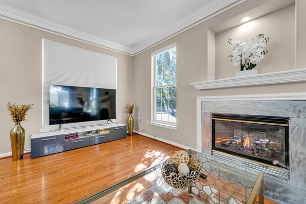 Una sala de estar con televisión de pantalla plana, chimenea y ventanas grandes.