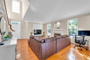 A spacious living room with a large sectional sofa, a fireplace, a television, and a desk with a computer.
