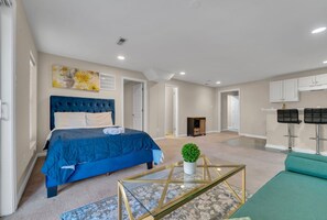Un salón amplio con una cama grande, una mesa de centro y un sofá. Se ve una chimenea y una zona de cocina al fondo.