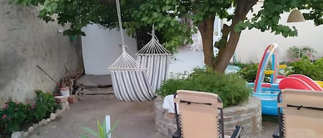 Un patio con una hamaca, dos sillas y una planta pequeña.