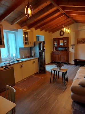 A modern kitchen with wooden beams, a dining area with a table and chairs, and a living room with a sofa. - Holiday Home 'Lilly Of Lemnos' with Shared Terrace, Private Garden and Air Conditioning (Ρουσσοπούλι)