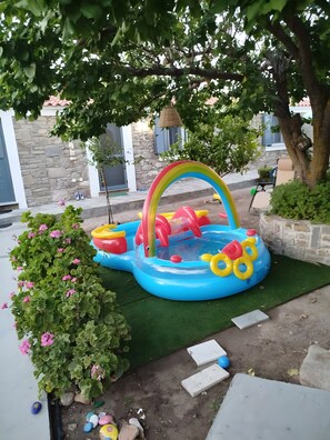 An inflatable pool with a rainbow arch, surrounded by greenery and a stone wall. - Holiday Home 'Lilly Of Lemnos' with Shared Terrace, Private Garden and Air Conditioning (Ρουσσοπούλι)