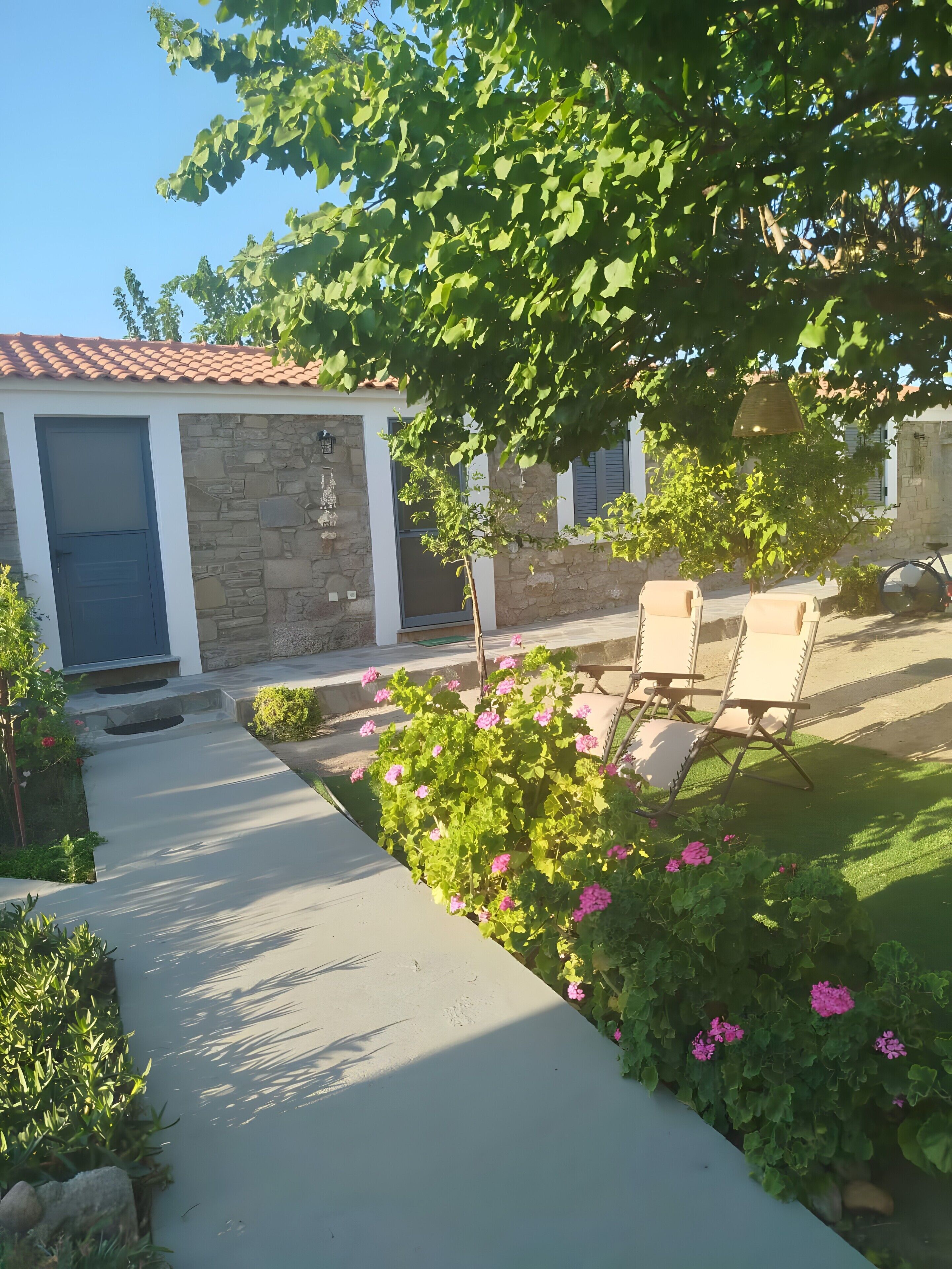 Una propiedad residencial con fachada de piedra, puerta azul, camino de entrada pavimentado y mobiliario exterior.