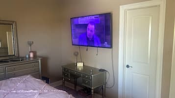 A bedroom with a bed, dresser, vanity, and a television mounted on the wall.