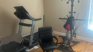 Ein Heimfitnessraum mit einem NordicTrack Laufband, einer Gewichtbank und einem Kabelzuggerät.