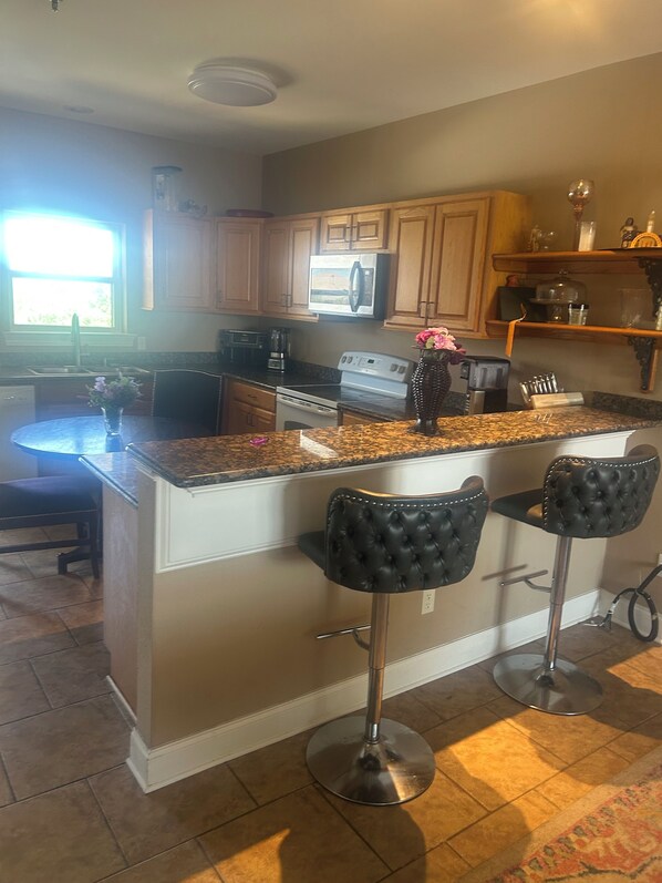 A kitchen with a central island, bar stools, wooden cabinets, and a window. - Cozy 1-bedroom condo in lovely Slidell with AC WiFi and fitness room (Slidell)