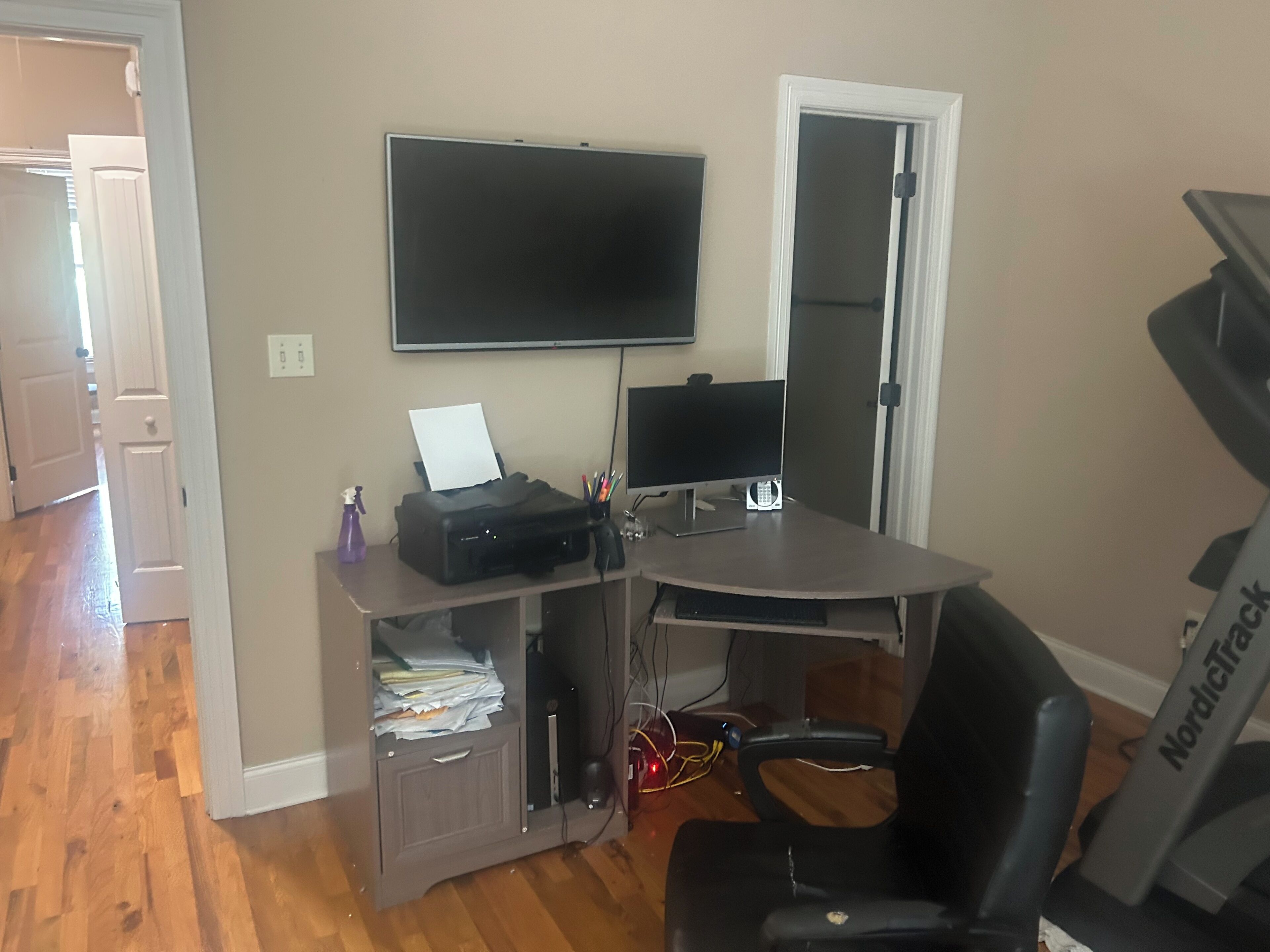 A home office setup with a desk, computer, printer, and a treadmill.