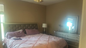 Ein Schlafzimmer mit Bett, Kommode, Nachttisch, Lampe und Deckenventilator.