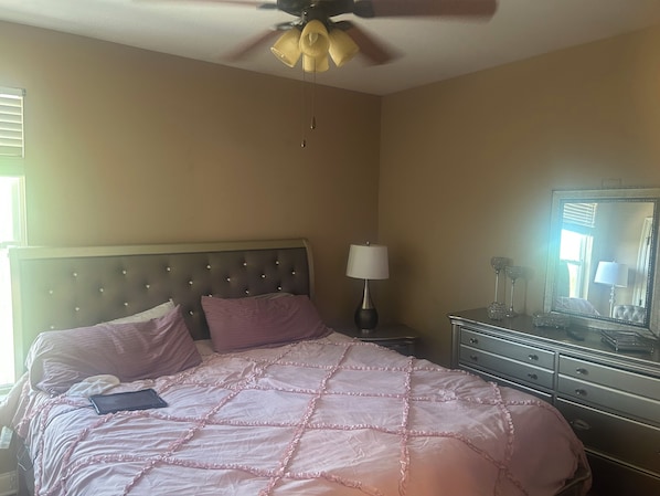 A bedroom with a bed, a ceiling fan, a bedside lamp, a dresser, and a mirror.