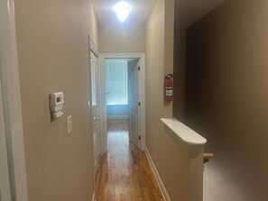 A hallway with a wooden floor, a white door, a fire extinguisher, and a white wall-mounted device.