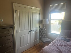 A bedroom with a bed, a chair, a dresser, and a window with blinds.
