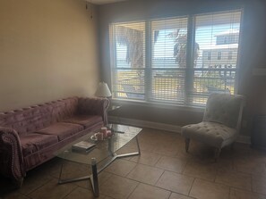 A living room with a sofa, armchair, glass coffee table, and a window with blinds.