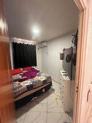 A bedroom with a bed, a desk, a wall-mounted air conditioner, and a curtain. - Cozy apartment (Manaus)
