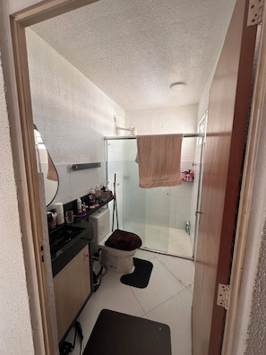 A compact bathroom with a glass shower enclosure, a toilet, and a sink area with toiletries. - Cozy apartment (Manaus)