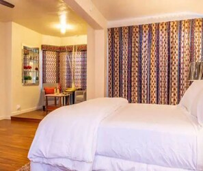 Quarto com cama grande, uma mesinha com cadeiras e cortina estampada.