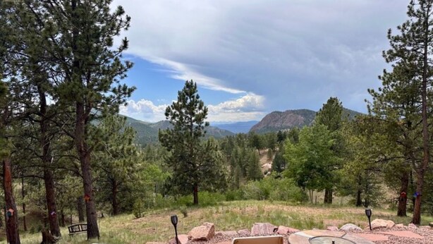 Un espace extérieur aménagé avec une table et des chaises, entouré d’arbres et offrant une vue sur un paysage montagneux.