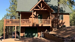 Une cabane en rondins à deux étages, dotée d’un balcon, d’un garage et d’un mur de soutènement en pierre.