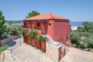 Un edificio rojo con una escalera de piedra que conduce a una puerta de madera, rodeado de vegetación y con vistas a una masa de agua.