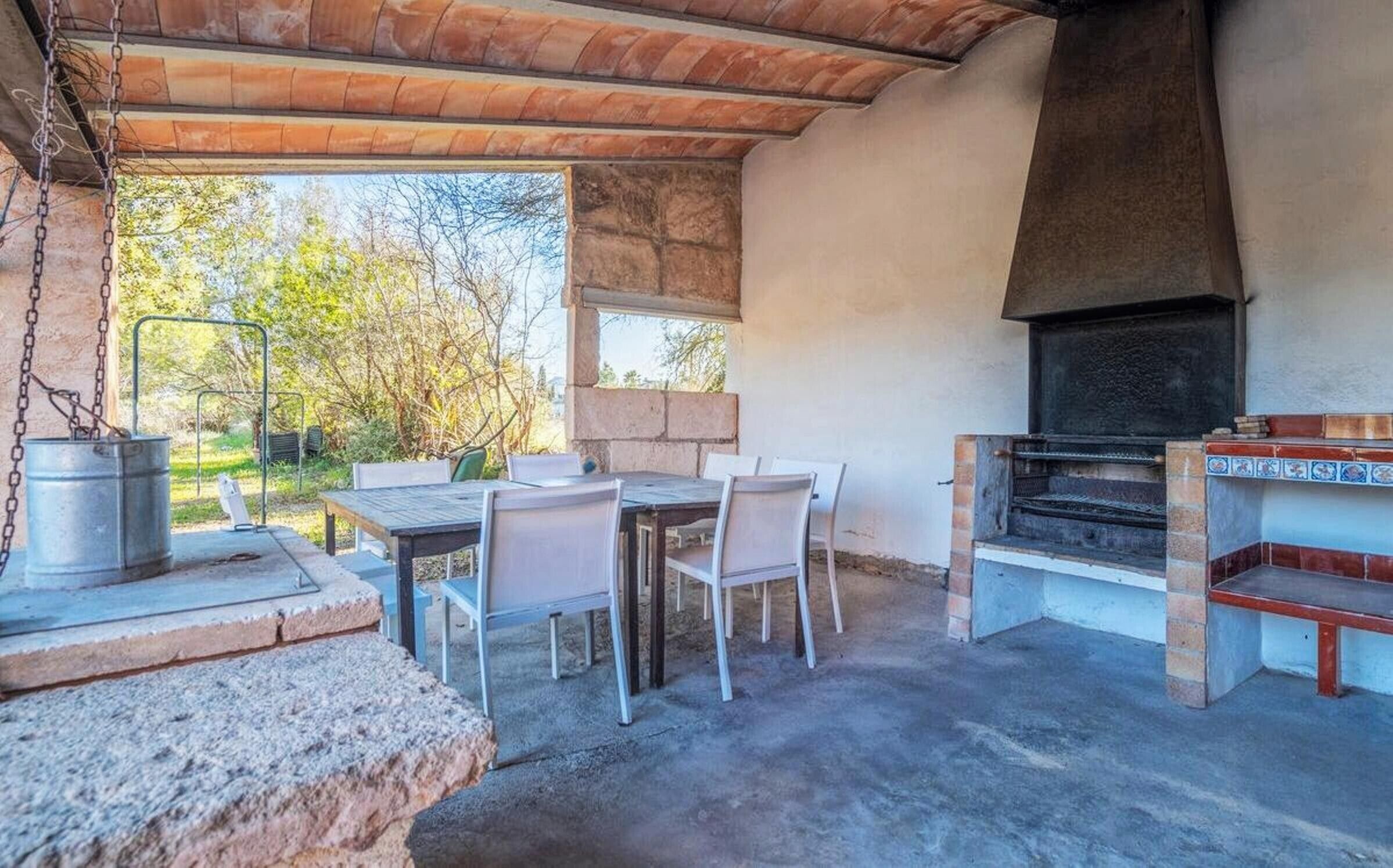 An outdoor patio with a table and chairs, a grill, and a view of trees.