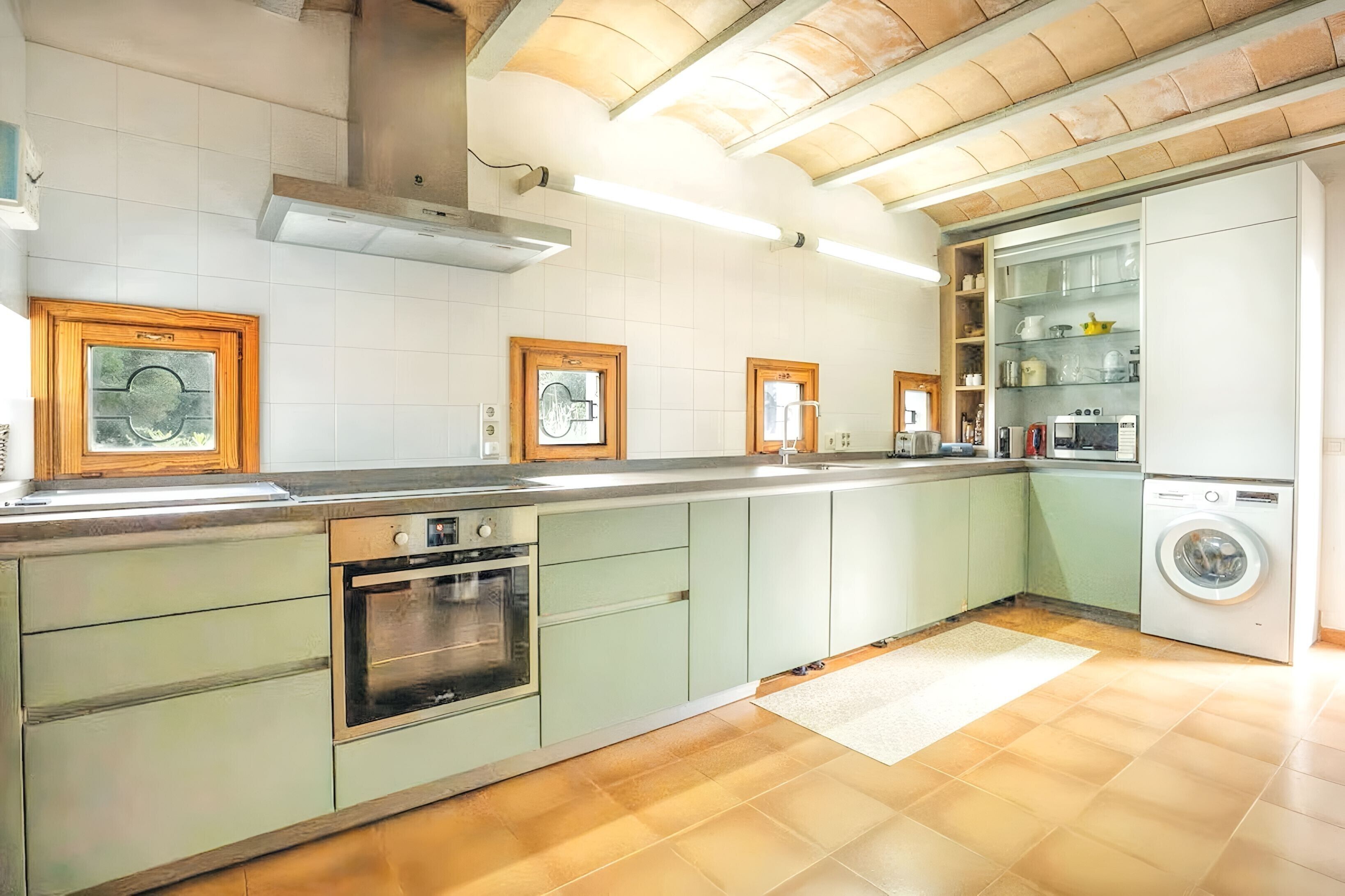 Een keuken met een inbouwoven, een wasmachine en een houten plafond.