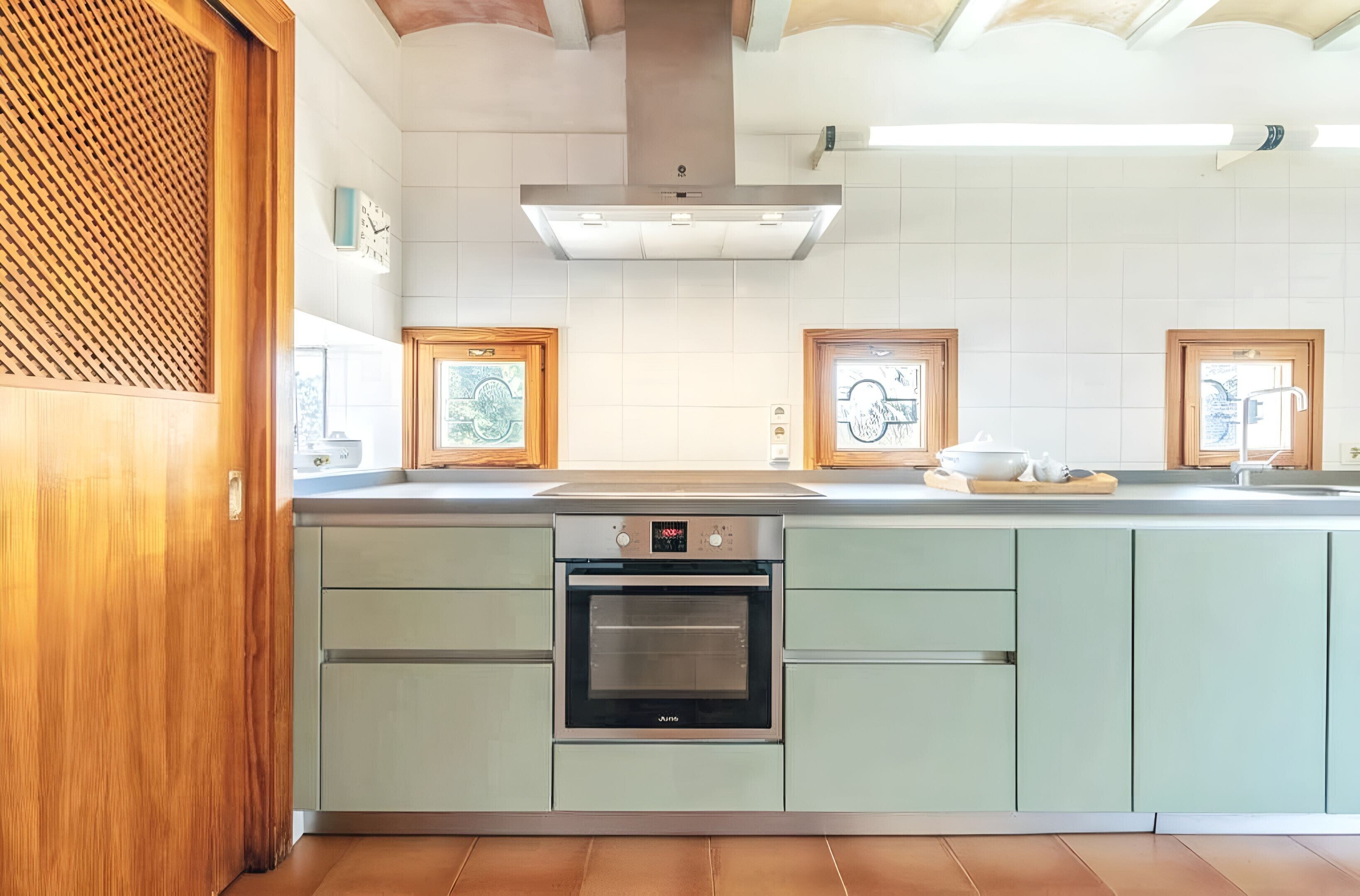 Une cuisine moderne dotée d’un four encastré, d’une hotte en acier inoxydable et de meubles de couleur vert clair.