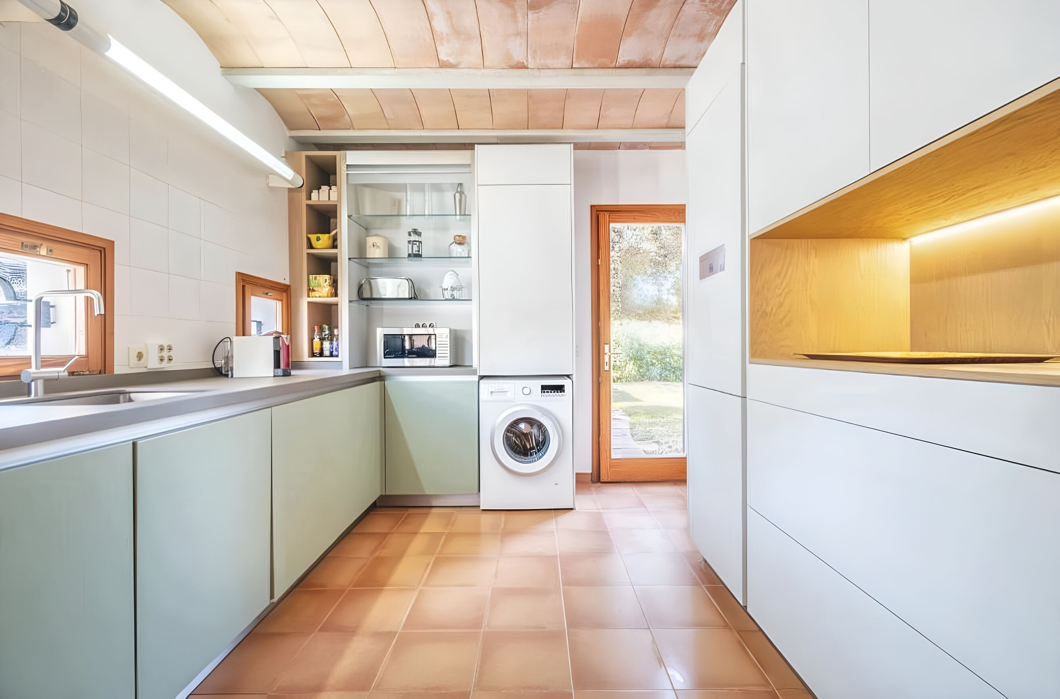 Une cuisine compacte équipée d’un lave-linge encastré, d’un évier et d’une petite fenêtre.