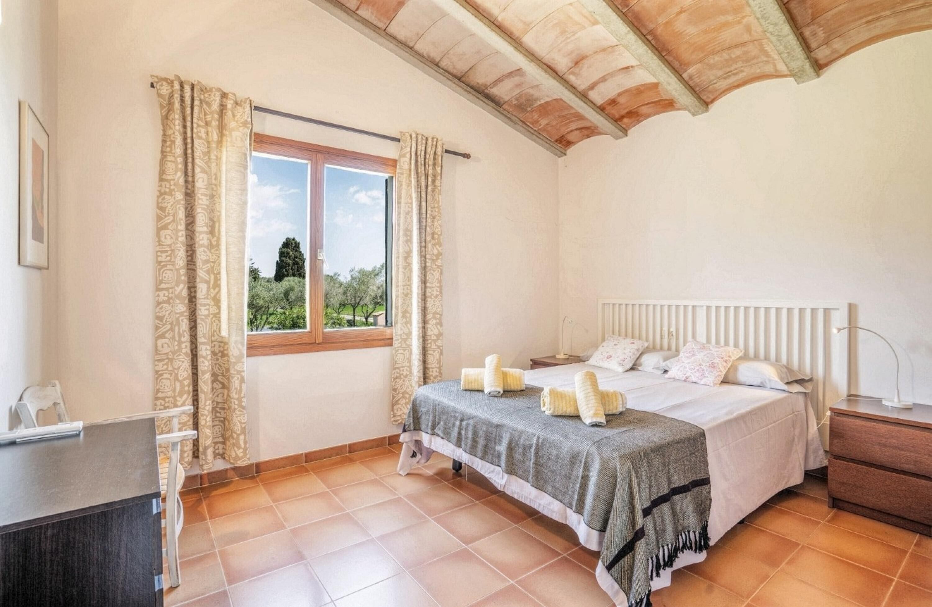 A bedroom with a large bed, a window with curtains, a desk, and a radiator.