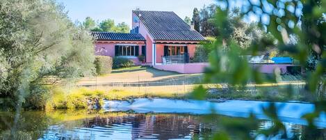 Une maison avec un toit en pente, un jardin et un étang.
