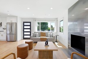 A modern kitchen with a built-in refrigerator, a dining area with a wooden table and chairs, and a living room with a sofa and a TV. - Newly Renovated Luxury Home near Stanford & Techs (East Palo Alto)