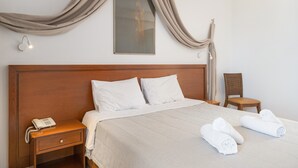 A hotel room with a wooden headboard, a bed with white linens, a bedside table with a phone, a chair, and a wall-mounted light fixture. - Classic Double Room at Hotel Aristotelis with Sea View and Balcony (Ancient Epidavros)