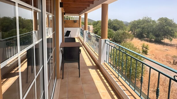Varanda coberta com vista para o campo, uma mesa e cadeiras.