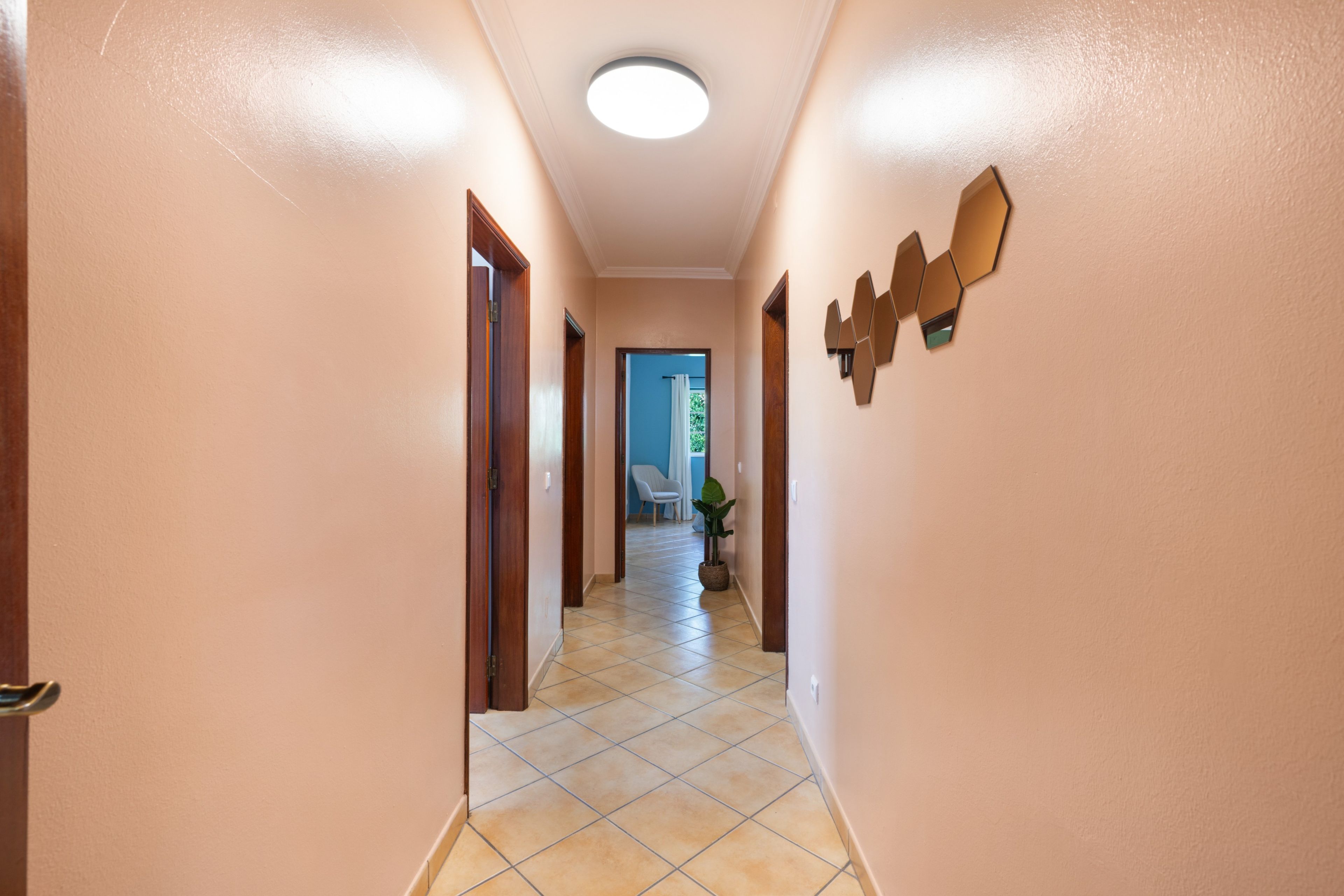 Un couloir avec un sol carrelé, des portes en bois et un luminaire au plafond.