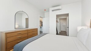 A bedroom with a bed, a dresser, a mirror, and an air conditioning unit. - Two Bedroom w/ Balcony | Modern Salt Lake City Stay | Central Downtown Location (Salt Lake City)