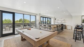 A modern indoor space with a pool table, bar area, and large windows offering a view of the outdoors.