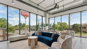A spacious, modern lounge area with large windows, comfortable seating, and a visible street sign indicating a nearby restaurant. - Modern Studio type Room in Salt Lake City | Near Downtown Location (Salt Lake City)