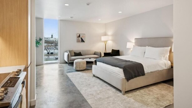 A modern bedroom with a large bed, a sofa, a small table, and a view of the city. - Modern Studio type Room in Salt Lake City | Near Downtown Location (Salt Lake City)